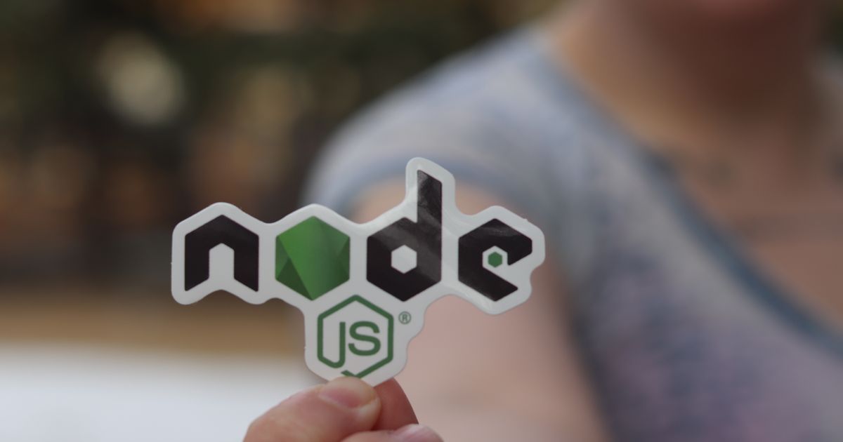 A person holding a Node.js logo sticker up to the camera, the background softly out of focus