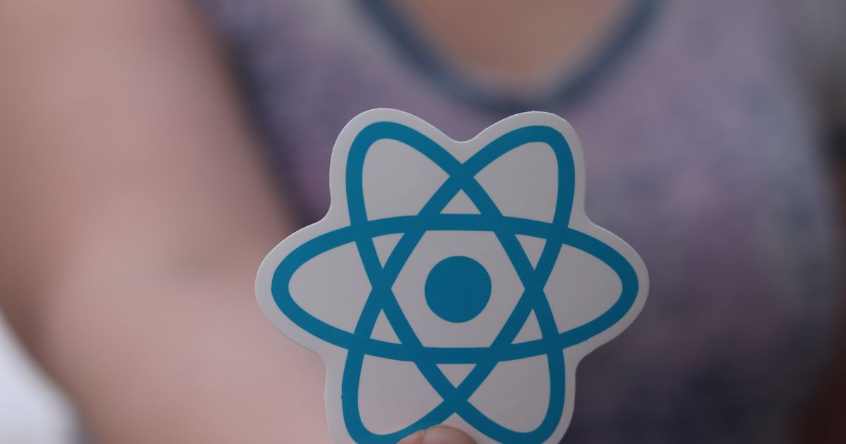 A person holding a React logo sticker between finger and thumb, the background softly blurred