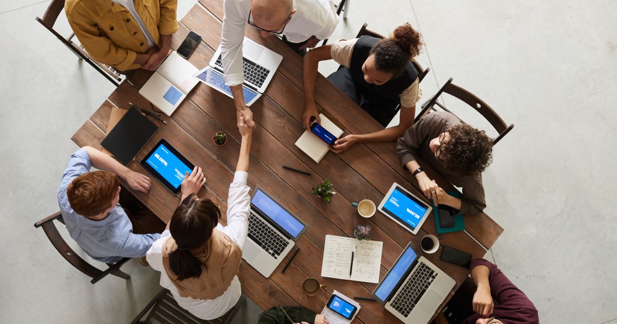 Two teams meeting around a table, shaking hands over laptops and notes